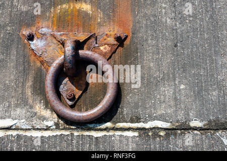 An old and rusty boat mooring ring set into the harbour concrete Stock Photo