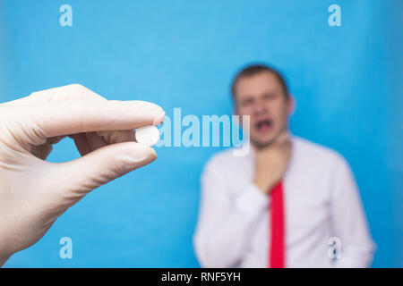 The doctor holds an antiseptic pill in his hand for a sore throat, in the background a man whose sore throat has a sore throat, a cure for sore throat Stock Photo