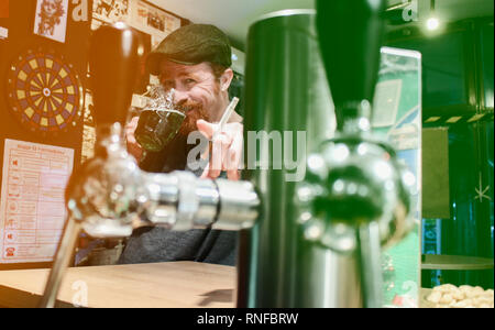 Good guy Irish smokes cigarette and drink beer and calling zou to join in pub during St Patrick Day (filter represent Irish flag) Stock Photo