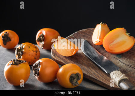 ripe and orange persimmons on cutting board with knife Stock Photo