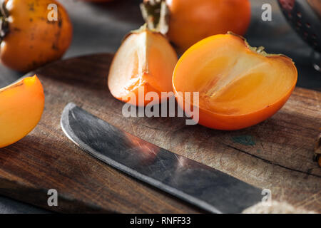 orange and sliced persimmons on cutting board with knife Stock Photo