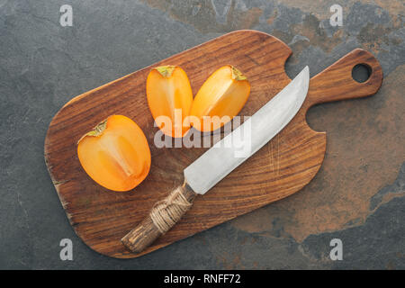 cut ripe tasty persimmons on cutting board with knife Stock Photo