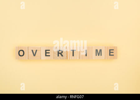 top view of overtime lettering made of wooden cubes on yellow background Stock Photo