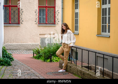 A young, beautiful, dark-haired woman standing at the basement staircase in an old home yard. Stock Photo