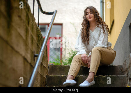 A young, beautiful, dark-haired woman sitting on an old house stairs. Copy space. Stock Photo