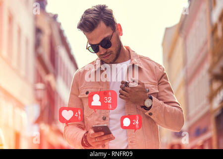 Young Fashionable Adult Man Using Social Media on Smartphone on The Street - Like, Follower, Comment Icons and Numbers Stock Photo