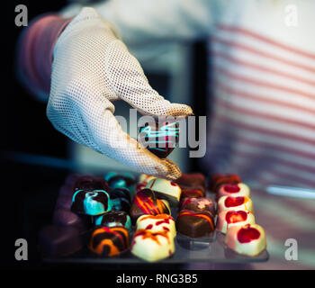 Chocolate heart shaped pralines in pastry shop, one of them in  hand with white glove. Stock Photo