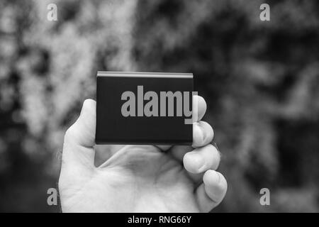 Man hand holding portable external hard drive disk with high read and write speed against green background unboxing testing - black and white Stock Photo
