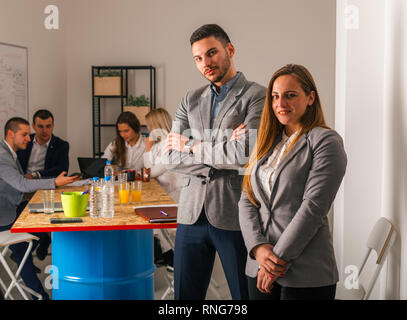 A portrait of a business man and a business woman in front of the meeting table while their team seats in the back. Stock Photo