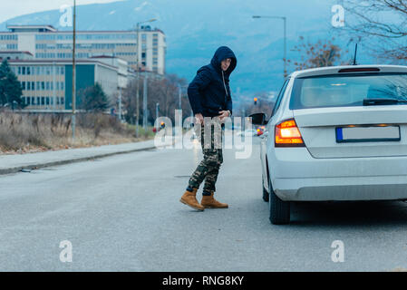 Gangster with a gun trying to rob a guy which is sitting in his car. Stock Photo