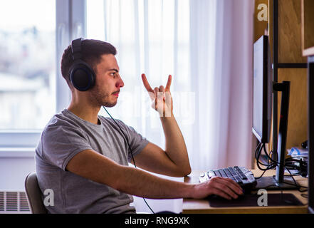 Handsome young man in t-shirt sitting and typing on computer keyboard at home Stock Photo