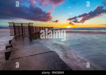 Long-exposure photo of waves crashing into McGurk Beach Jetty at sunset with colorful clouds in the sky, Toes Beach, Playa Del Rey, California Stock Photo