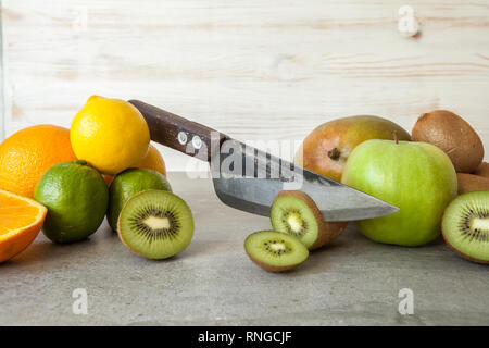 Fresh citrus fruits, half cut kiwi orange and lemons on cutting board with knife on stone background. Stock Photo