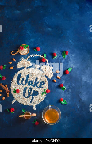 Alarm clock with Wake Up words written with oatmeal, raspberries and cinnamon. Healthy eating concept on a dark background with copy space. Stock Photo