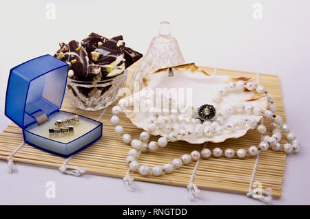Still life with jewelry, some earrings and a pearl necklace with some chocolate bark in the background Stock Photo