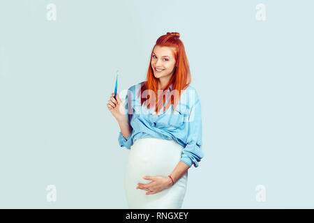 Wonderful happy redhead woman in expectancy smiling at camera while holding toothbrush isolated on light blue background. Stock Photo