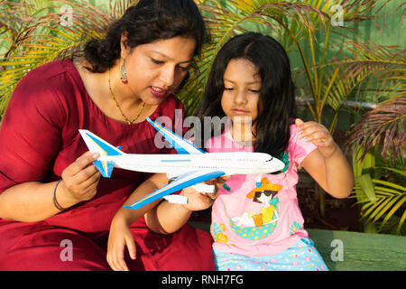 Mother showing her daughter a toy airplane while little girl observing it carefully, Pune Stock Photo