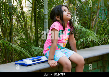 Small Indian girl upset looking upwards with her toy laptop by her side, Pune Stock Photo