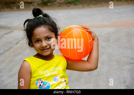 Small Indian girl holding a ball on her shoulder with happy expression, Pune Stock Photo