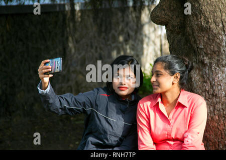 Two young Indian girls sitting and taking selfie with happy expression, Pune Stock Photo
