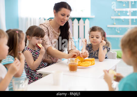 Children and carer together eating fruits in kindergarten or daycare Stock Photo