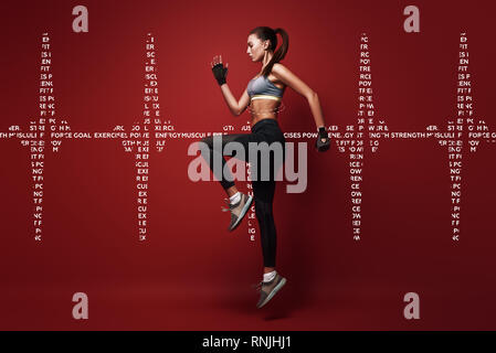 Full length portrait of a healthy muscular sportswoman jumping  over red background. Dynamic movement. Side view Stock Photo