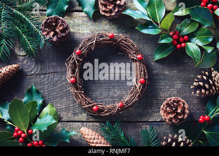 Making Christmas wreath using fresh and all natural materials. Christmas wreath with red berries and cones on wooden table. Stock Photo