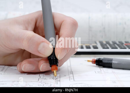 Woman's hand holding rapidograph, architectural plans in background Stock Photo