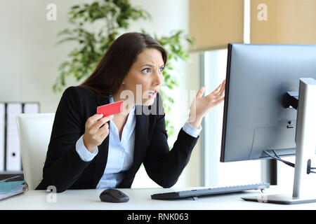 Confused office worker trying to pay online with credit card on a desktop computer Stock Photo