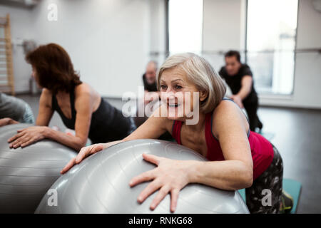 Group of cheerful female seniors in gym doing exercise on fit balls. Stock Photo