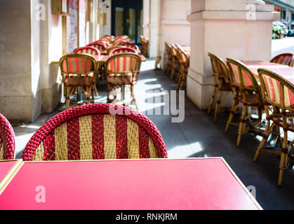Typical terrace outside a parisian cafe with red melamine tables and rattan chairs under the arches in the sunshine. Stock Photo