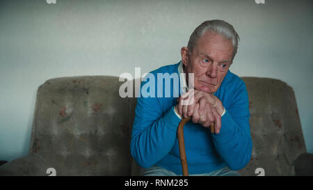 Portrait of a senior man looking sad while leaning on his walking stick. Stock Photo