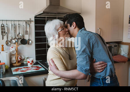 Teenage boy is smiling for the camera while his grandmother kisses his cheek. Stock Photo