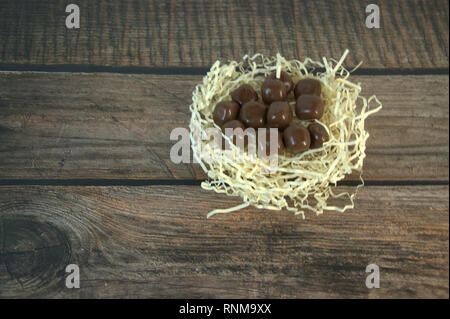 A nest of straw with chocolates and and decorative balls on a wooden table. Close-up. Stock Photo