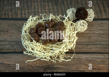 A nest of straw with chocolates and and decorative balls on a wooden table. Close-up. Stock Photo