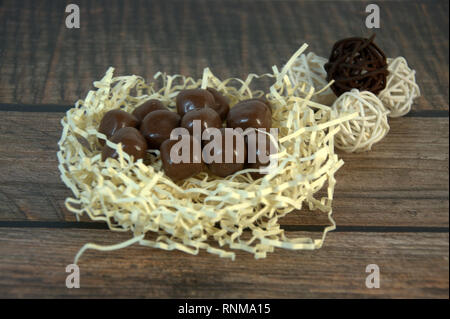 A nest of straw with chocolates and and decorative balls on a wooden table. Close-up. Stock Photo