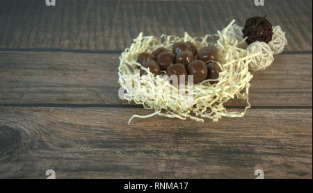 A nest of straw with chocolates and and decorative balls on a wooden table. Close-up. Stock Photo
