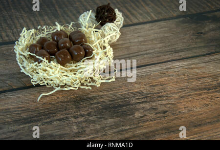 A nest of straw with chocolates and and decorative balls on a wooden table. Close-up. Stock Photo