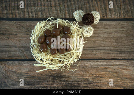 A nest of straw with chocolates and and decorative balls on a wooden table. Close-up. Stock Photo