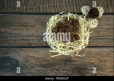 A nest of straw with chocolates and and decorative balls on a wooden table. Close-up. Stock Photo