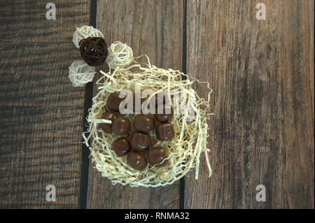 A nest of straw with chocolates and and decorative balls on a wooden table. Close-up. Stock Photo