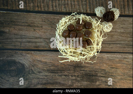 A nest of straw with chocolates and and decorative balls on a wooden table. Close-up. Stock Photo