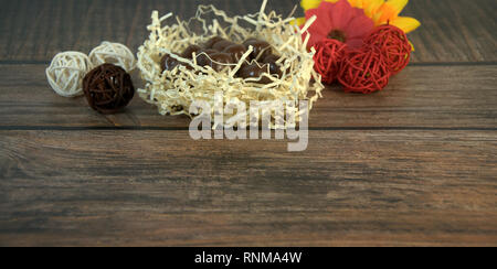 Round chocolates in a nest of straw, multicolored decorative balls and flower buds on a wooden table. Close-up. Stock Photo
