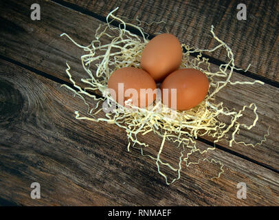 Three chicken eggs in a nest of straw on a wooden table. Close-up. Stock Photo