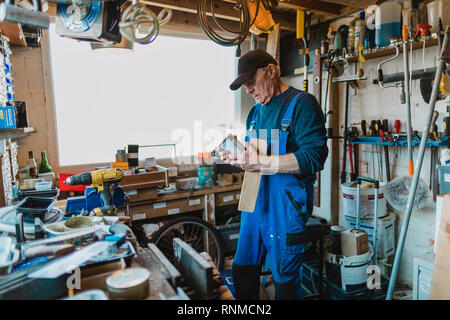 Senior man is working in his shed and is reading the label on a varnish. Stock Photo