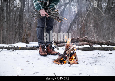 Making a campfire in a snowy forest. Male person near a fire on a winter day in the woods Stock Photo