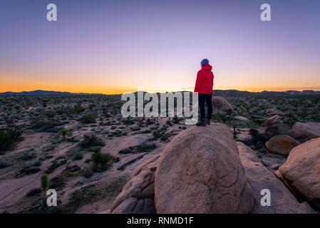 Young woman standing on granite rocks, at sunset, rock formations, White Tank Campground, Joshua Tree National Park