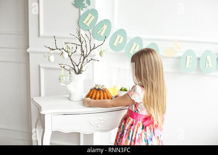 A blonde girl in a beautiful colored dress is standing with her back to the festive table holding a festive cupcake Stock Photo