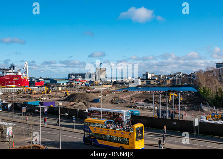 Construction work on building site at Waterfront Plaza with tourists in open top bus and ships in harbour, Victoria Quay, Leith, Edinburgh, Scotland, Stock Photo