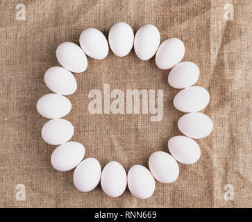 White chicken eggs lie in circle on rough canvas. Stock Photo